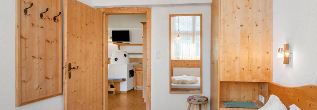 A cozy bedroom with wood paneling and a large bed. The door leads to a bright bathroom. - Garni Nadine - Sölden