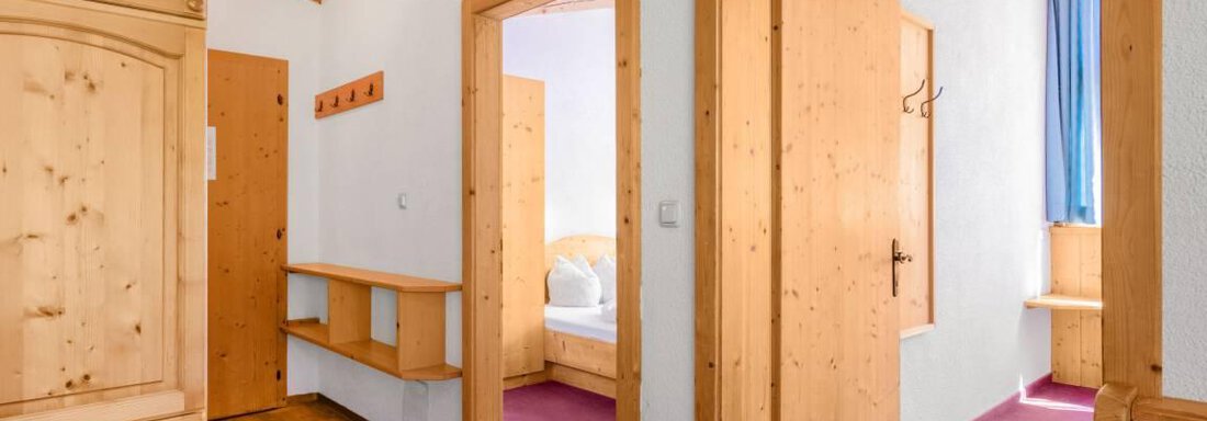 A cozy hallway with wooden furniture and two open doors. The floor is made of wood and the carpet is pink. - Garni Nadine - Sölden