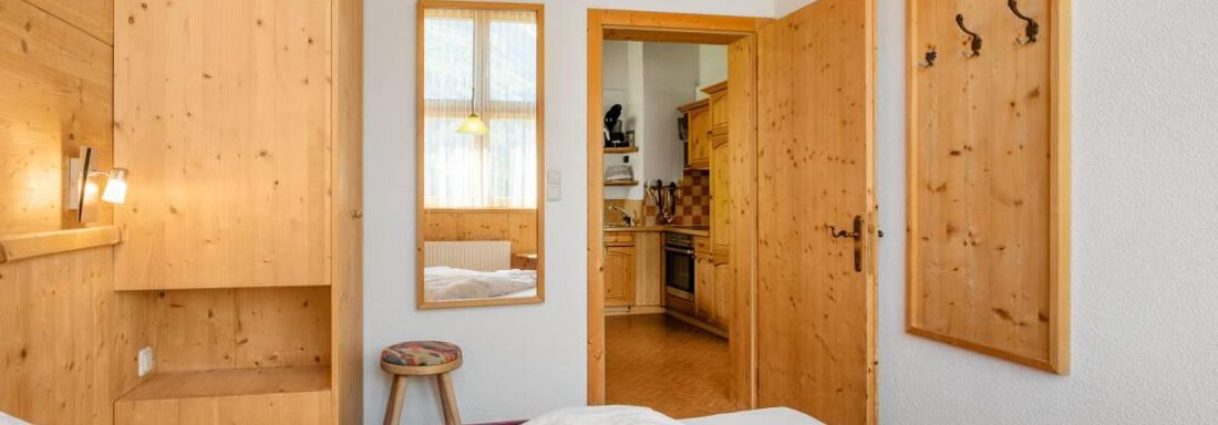 A cozy room with wooden paneling and a double bed. The doors lead to another room and the windows provide plenty of daylight. - Garni Nadine - Sölden