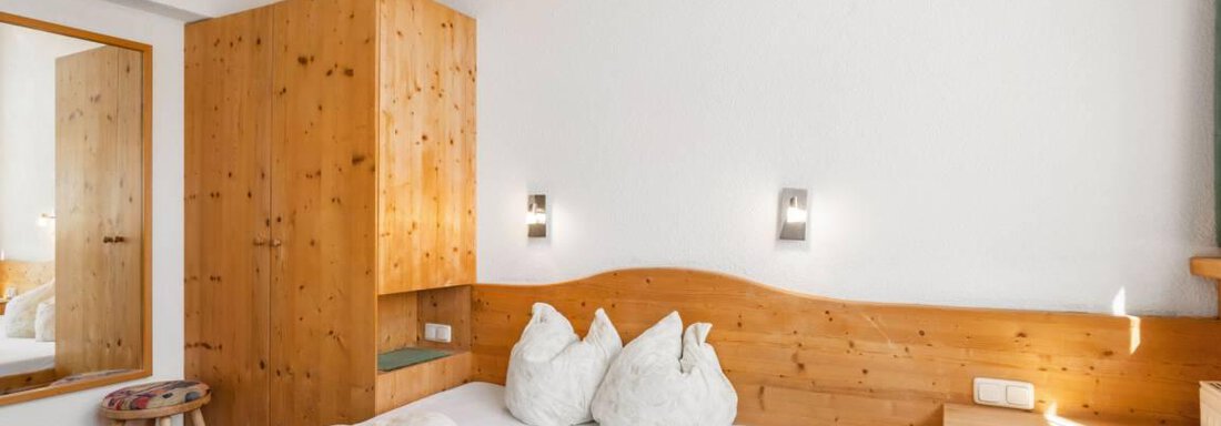 A cozy bedroom with wood paneling and a large bed. There is a mirror and modern lighting that creates an inviting atmosphere. - Garni Nadine - Sölden