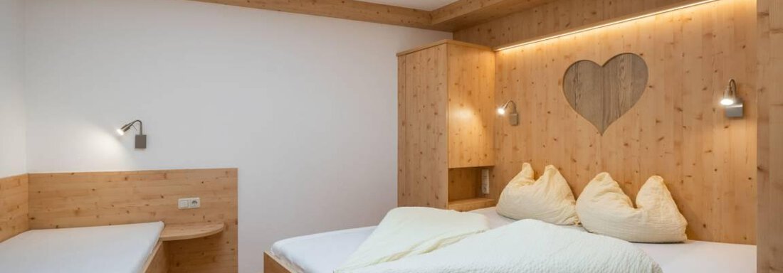 A cozy bedroom with wooden furniture and a large double bed. On the wall, there is a heart-shaped window that creates a charming atmosphere. - Garni Nadine - Sölden