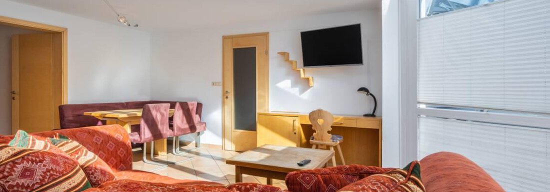 A bright living room with large windows and modern furniture. There is a cozy couch and a table in the room. - Garni Nadine - Sölden