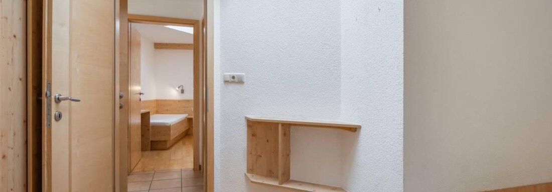 A simple room with a wooden floor and two beds. The open door in the background leads to another room. - Garni Nadine - Sölden