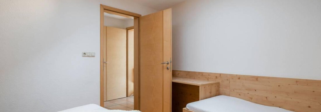 A simple bedroom with two beds and a light wood decor. A skylight provides ample daylight. - Garni Nadine - Sölden