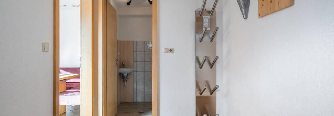 A bright entrance area with tiled flooring and wooden shelves. In the background, two doors and a sink are visible. - Garni Nadine - Sölden