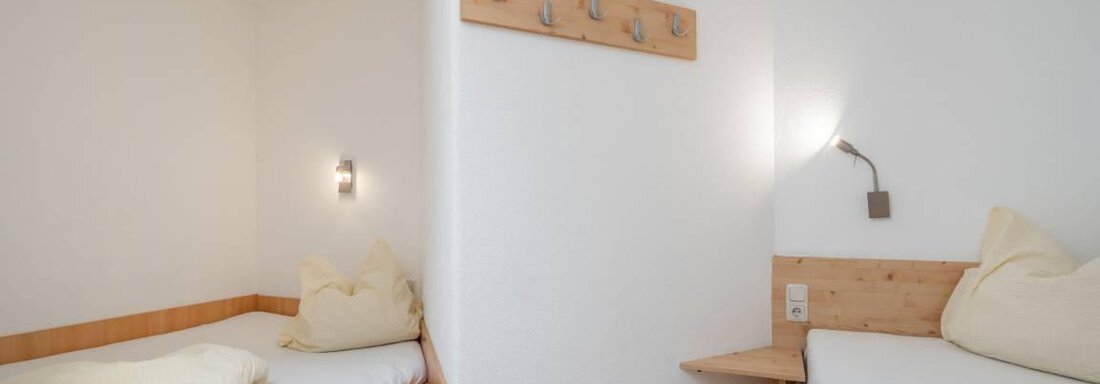 A simple bedroom with two single beds. The walls are light, and there is wood paneling as well as some wall hooks. - Garni Nadine - Sölden