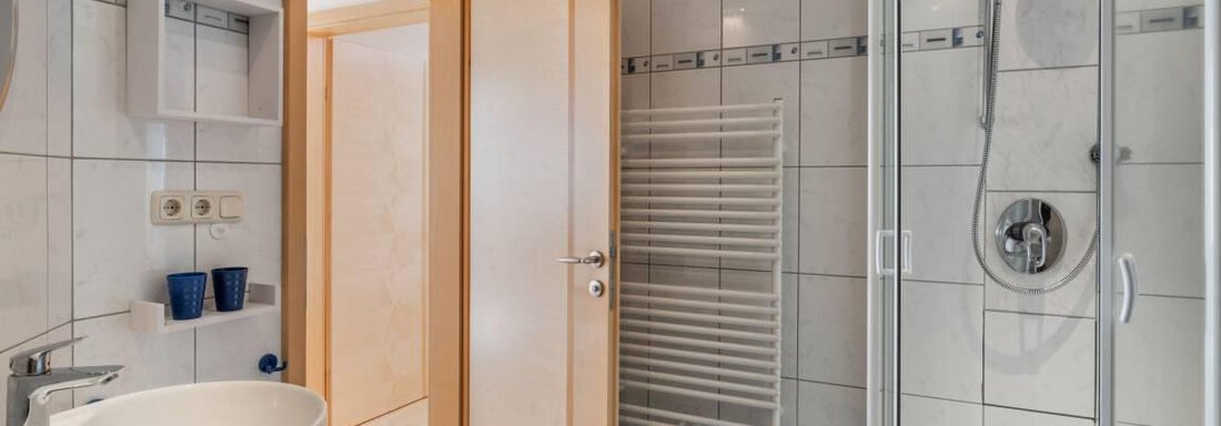 A modern bathroom with a shower, a sink, and a towel warmer. The walls are brightly tiled and there is an open door to another room. - Garni Nadine - Sölden