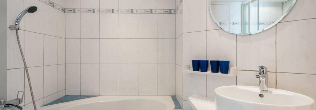 A modern bathroom with a bathtub and a sink. The walls are tiled in light colors and there is a large mirror. - Garni Nadine - Sölden