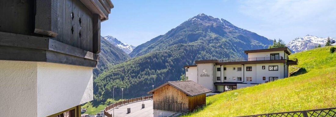 A picturesque mountain landscape with green meadows and tall mountains. In the foreground, charming wooden buildings can be seen. - Garni Nadine - Sölden