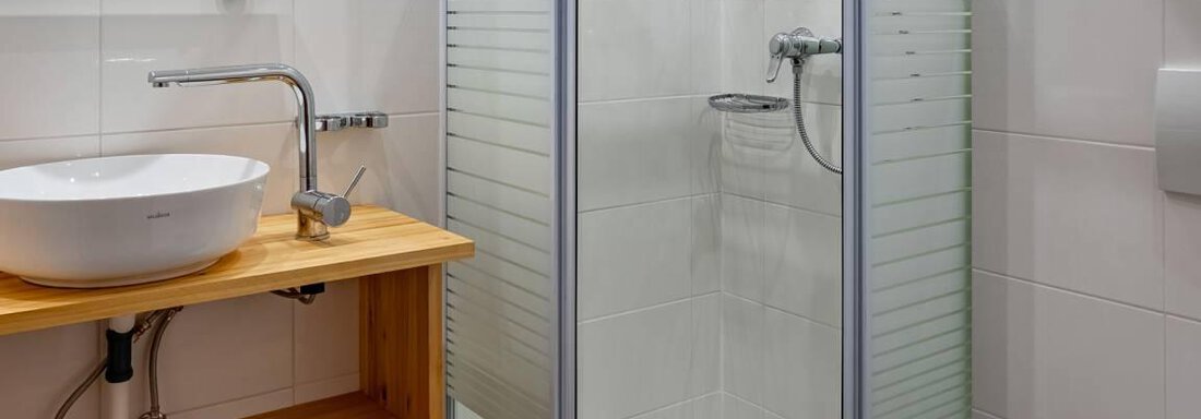 A modern bathroom with a shower and a handcrafted wooden shelf. The walls are light tiled and the sink is elegantly designed. - Garni Nadine - Sölden