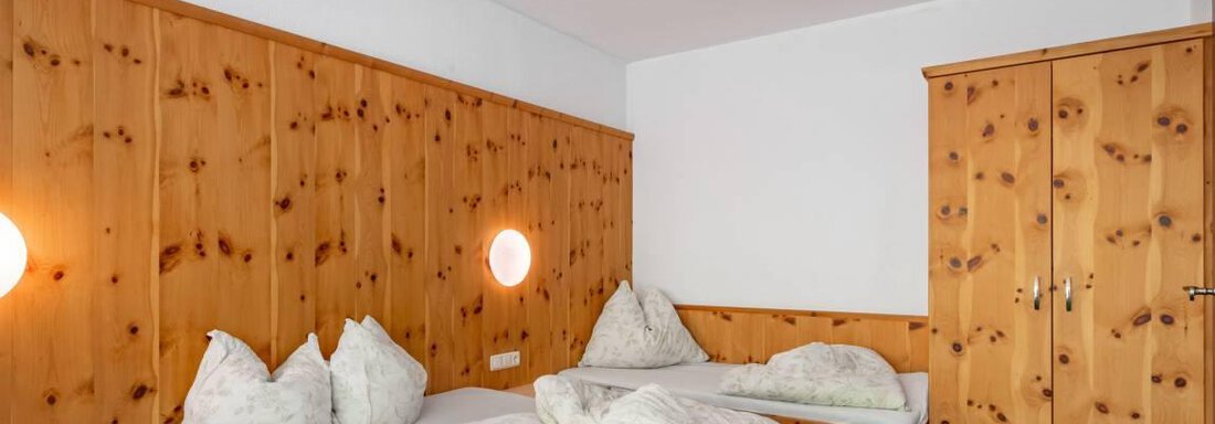 A simple bedroom with wooden paneling. There are two beds and a wardrobe. - Garni Nadine - Sölden