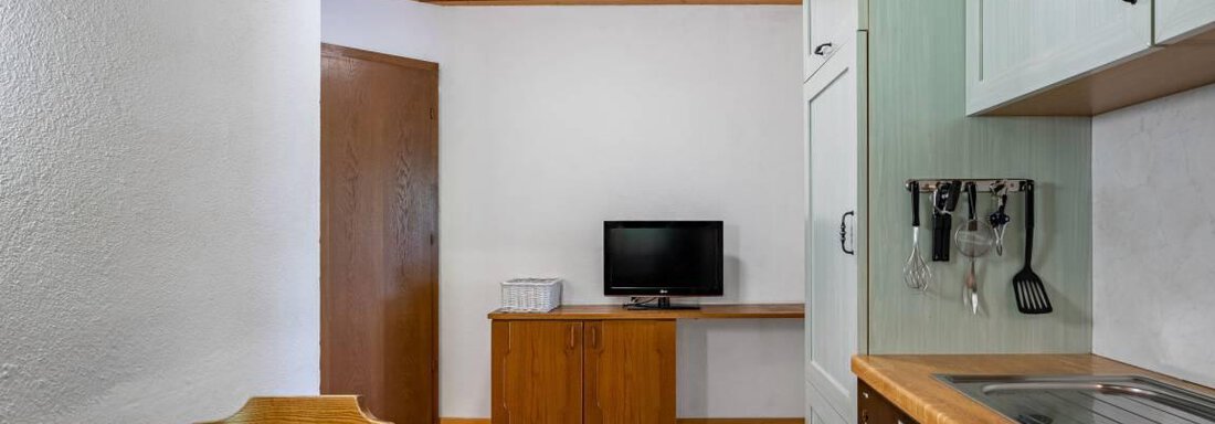 A bright, cozy kitchen room with a table and chairs. The integrated kitchen has modern furnishings and a television on the wall. - Garni Nadine - Sölden