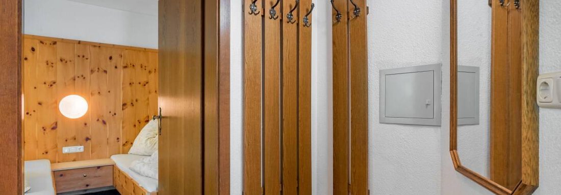 A bright hallway with wooden paneling and a large mirror. Some coat hooks hang on the wall, and the door leads to a bedroom. - Garni Nadine - Sölden