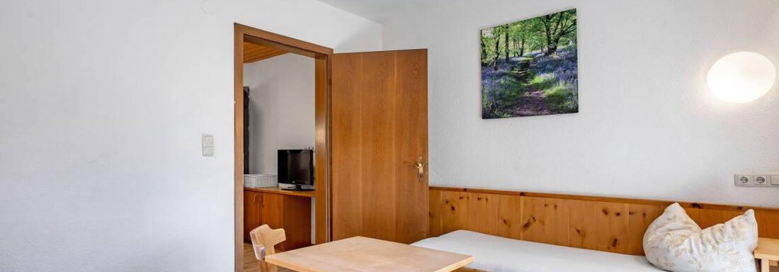A simple room with wooden furniture and two beds.  
A picture of a landscape hangs on the wall and a table with chairs is available. - Garni Nadine - Sölden