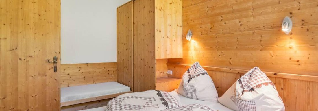 A cozy bedroom with wood paneling and a double bed. There are two pillows and a wooden dresser in the room. - Garni Nadine - Sölden