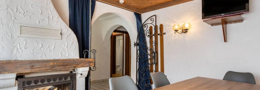 Appartement Alpenrose A cozy living space with a wood stove and a dining table group. The walls are light and adorned with wooden elements. - Garni Nadine - Sölden