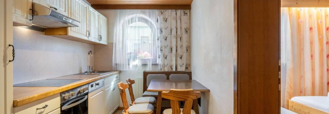 A cozy kitchen with wooden shelves and a seating area. The room has a warm, inviting atmosphere. - Garni Nadine - Sölden