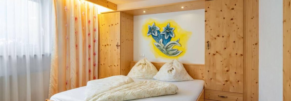 A cozy bedroom with a wooden bed and a colorful mural. The room has plenty of natural light and a calm atmosphere. - Garni Nadine - Sölden