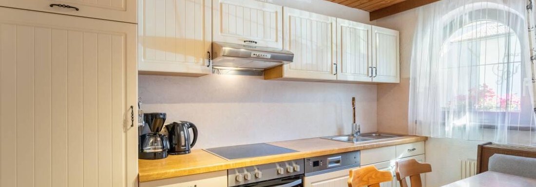 A modern kitchen with light furniture and a wooden ceiling. The room is well-lit and includes a dining table. - Garni Nadine - Sölden