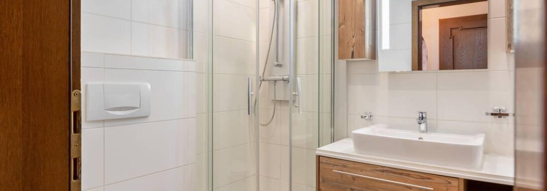 A modern bathroom with a round shower and an elegant sink. The walls are decorated with white tiles and wood paneling. - Garni Nadine - Sölden