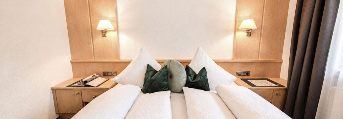 A cozy hotel room with two beds and modern wooden furniture. The pillows and soft lighting create an inviting atmosphere. - Garni Rustica - Sölden