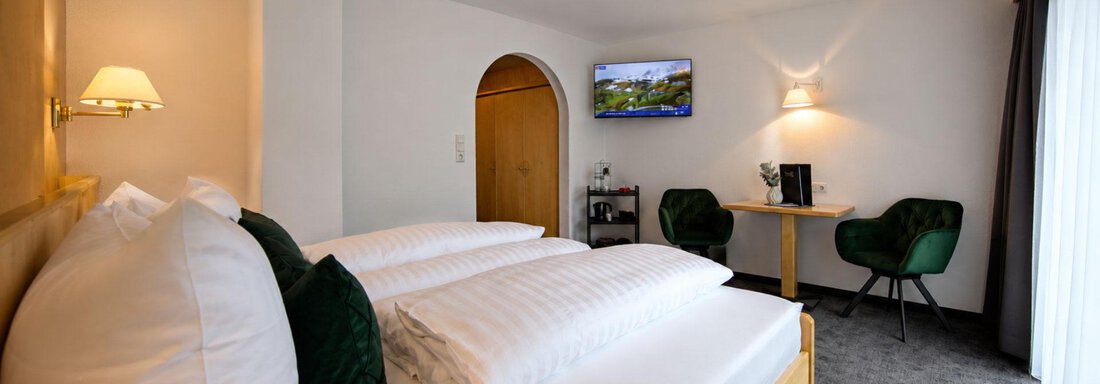 A modern room with two bedrooms and soft pillows. In the corner, there is a table with chairs and a television on the wall. - Garni Rustica - Sölden