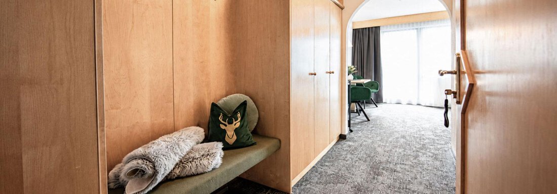 A spacious hallway with wooden furniture and a cozy sitting area. At the end of the hallway, there is a window that lets in natural light. - Garni Rustica - Sölden