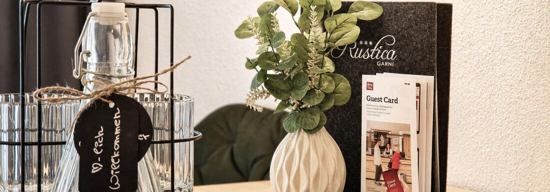 A stylish table with a decorative vase and a plant. Next to it is a bottle of water and an informational booklet for guests. - Garni Rustica - Sölden