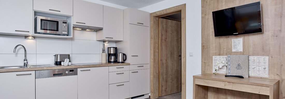 A modern kitchen with bright cabinets and a microwave. There is a television on the wall and a wooden table. - Gästehaus Bergkristall - Sölden