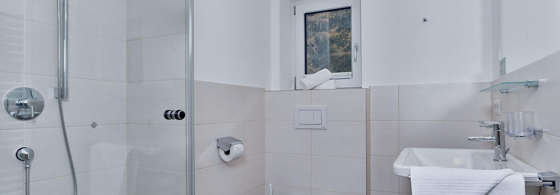 A modern bathroom with a shower and toilet. The walls are tiled in light colors and there is a large window. - Gästehaus Bergkristall - Sölden
