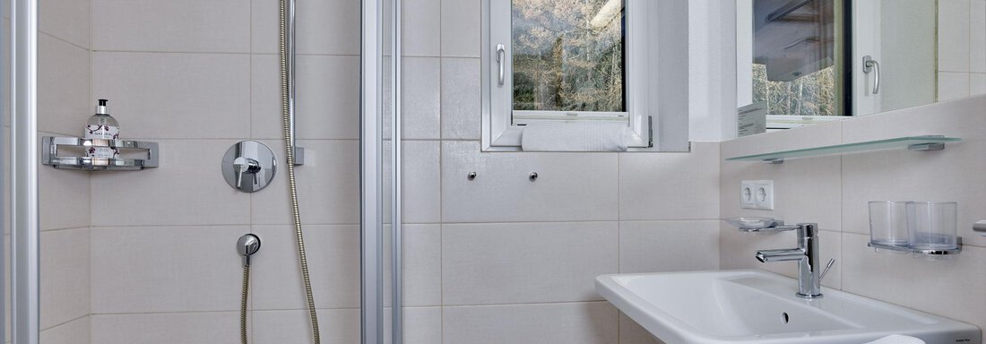 A modern bathroom with a shower and sink. A window lets in natural light. - Gästehaus Bergkristall - Sölden