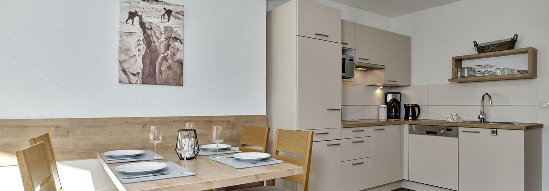 A bright, modern kitchen with a dining area. The table is set and the decor is in neutral colors. - Gästehaus Bergkristall - Sölden