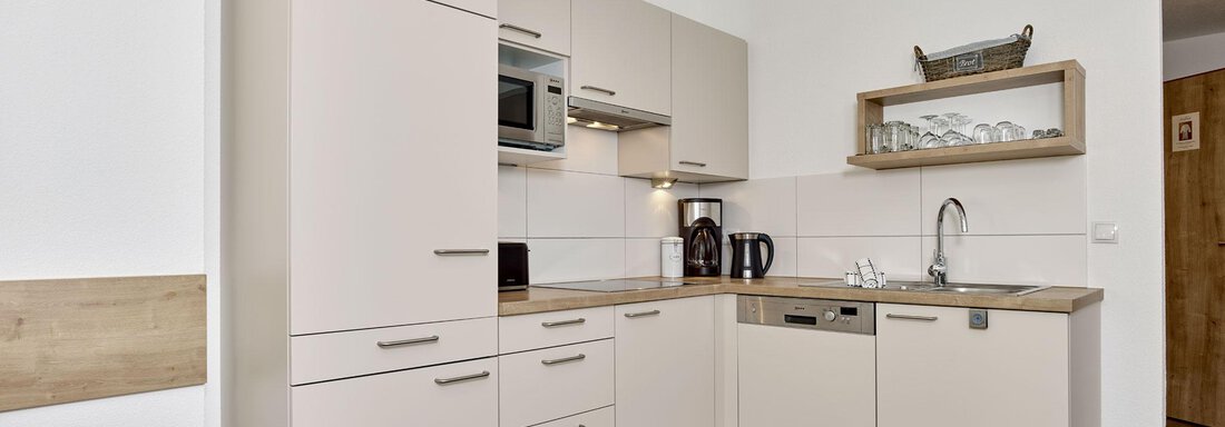 A modern kitchen with bright cabinets and a wooden surface. It is functionally furnished and has various appliances such as a microwave and a dishwasher. - Gästehaus Bergkristall - Sölden