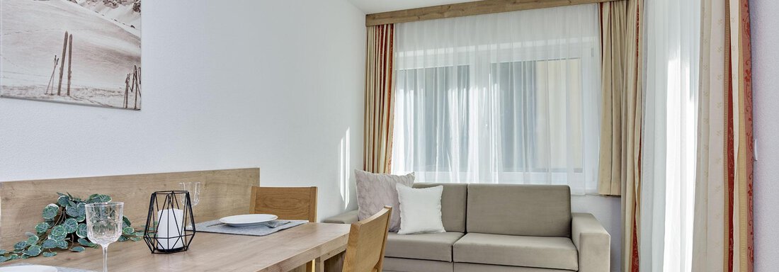 A bright living room with a dining area and a comfortable couch. Large windows let in plenty of light and create an inviting atmosphere. - Gästehaus Bergkristall - Sölden