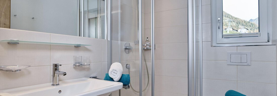 A modern bathroom with a shower and a sink. There are bright tiles and a small window opening that lets in light. - Gästehaus Bergkristall - Sölden