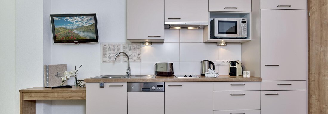 A modern kitchen with bright cabinets and a wooden countertop. There are appliances like a refrigerator, a microwave, and a dishwasher. - Gästehaus Bergkristall - Sölden