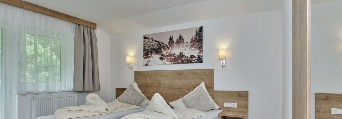 A modern room with two single beds and wooden paneling. The windows let in bright light and a decorative picture adorns the wall. - Gästehaus Bergkristall - Sölden