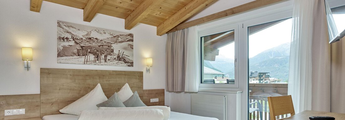 A modern bedroom with wooden ceilings and large windows. The room is comfortably furnished and offers a view of the surrounding mountains. - Gästehaus Bergkristall - Sölden
