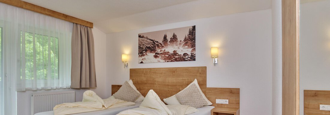 A bright and modern bedroom with two single beds. The walls are painted in neutral colors, and a large window lets in plenty of light. - Gästehaus Bergkristall - Sölden
