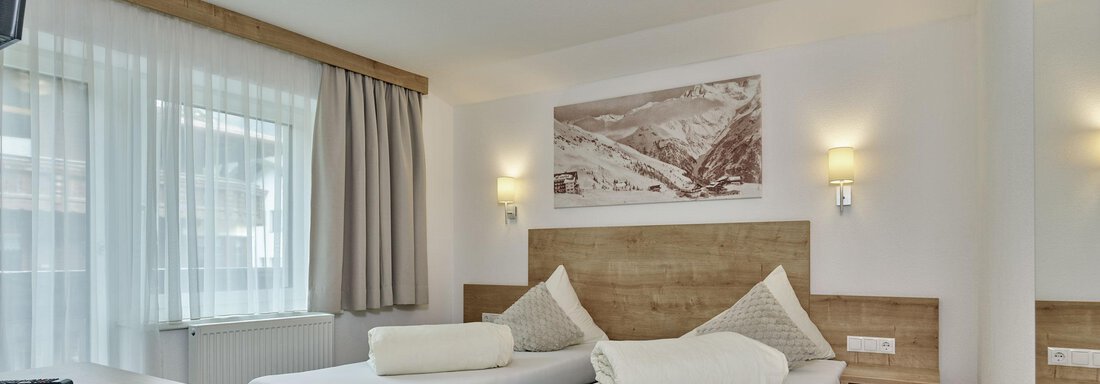 A cozy hotel room with two single beds and modern wooden design. Large windows provide plenty of daylight and an inviting atmosphere. - Gästehaus Bergkristall - Sölden