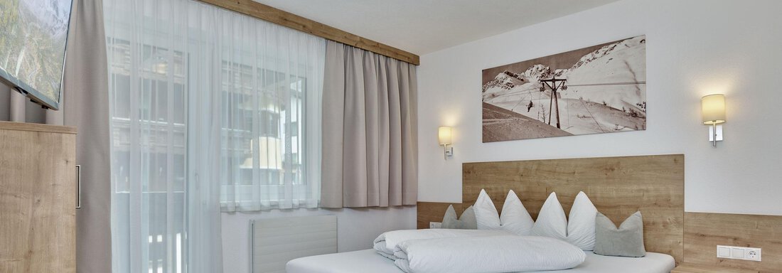 A modern bedroom with a large bed and wooden furniture. The room has a bright atmosphere and a view of nature. - Gästehaus Bergkristall - Sölden