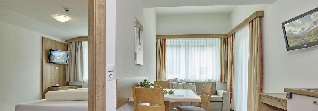 A modern room with a bed, a table, and chairs. Bright windows let in a lot of light and create an inviting atmosphere. - Gästehaus Bergkristall - Sölden