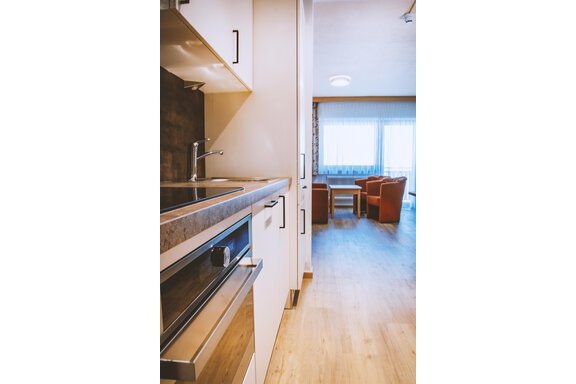 A modern kitchen with a stove and sink. In the background, there is a cozy living area with a table and chairs. - Gästehaus Europa - Sölden