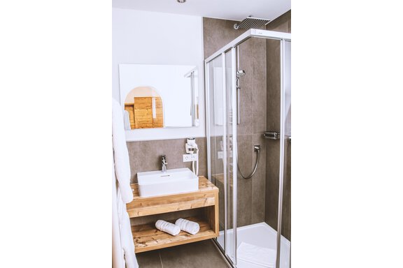 A modern bathroom with a glass shower and a wooden vanity. Fresh towels are neatly arranged on a shelf. - Gästehaus Europa - Sölden