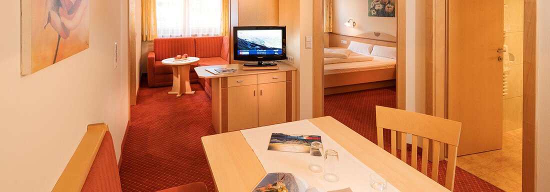 A cozy living area with a table, a television, and seating. The warm colors and harmonious decor create an inviting atmosphere. - Gästehaus Europa - Sölden