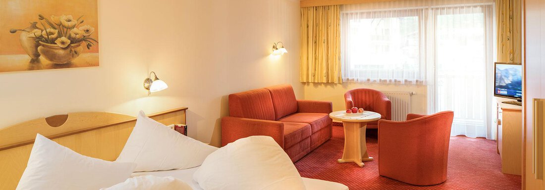 A cozy hotel room with a double bed, a sofa, and a small table. It has large windows that let in plenty of light. - Gästehaus Europa - Sölden