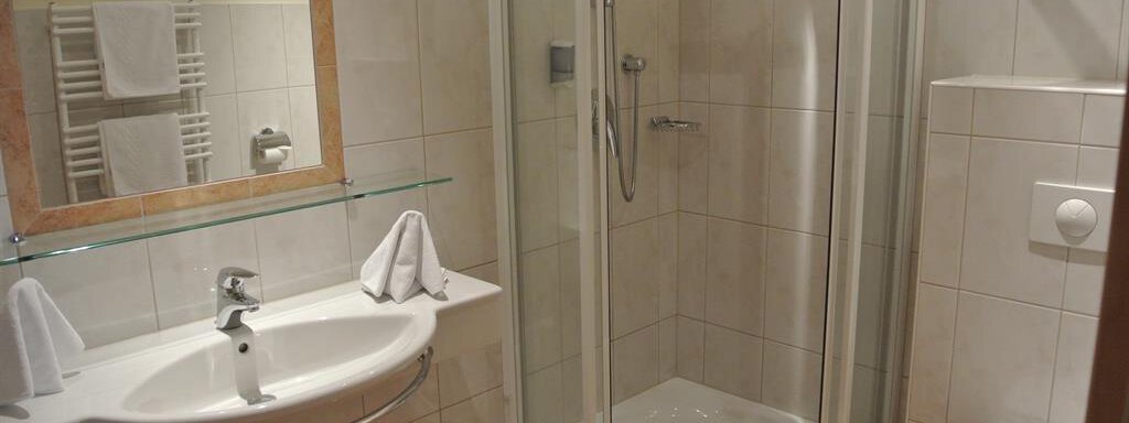 A modern bathroom with a shower, a sink, and a toilet. Towels are neatly folded and a mirror is mounted on the wall. - Gästehaus Europa - Sölden