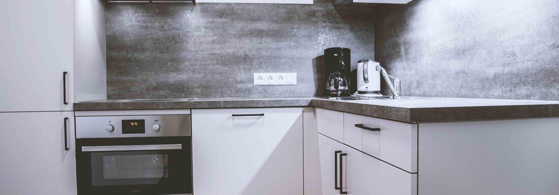 A modern kitchen with white cabinets and a dark countertop. The equipment includes a stove, a coffee maker, and a kettle. - Gästehaus Europa - Sölden