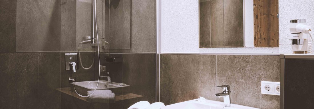 A modern bathroom with a walk-in shower and an elegant porcelain sink. The walls are in tasteful dark gray, and fresh towels are ready. - Gästehaus Europa - Sölden