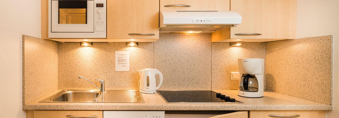 A modern kitchen with wooden cabinets and a bright countertop. There is a microwave, a kettle, and a coffee machine. - Gästehaus Europa - Sölden